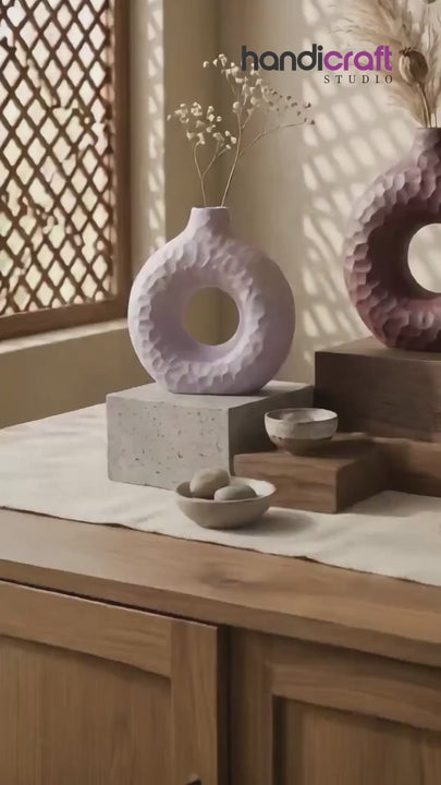 Ceramic vase in donut form placed on a mantel beside framed art and dried stems