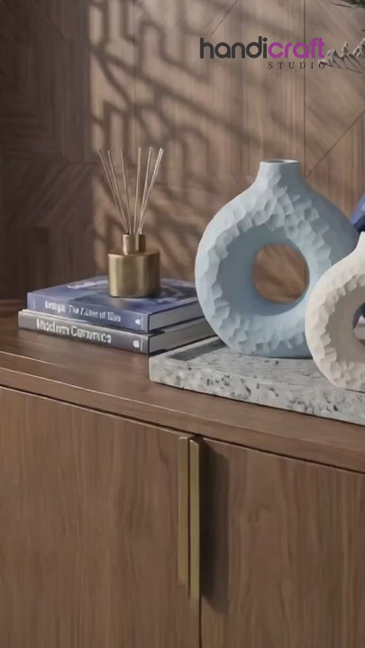 Matte donut vase in a soft tone holding dried stems on a linen covered table